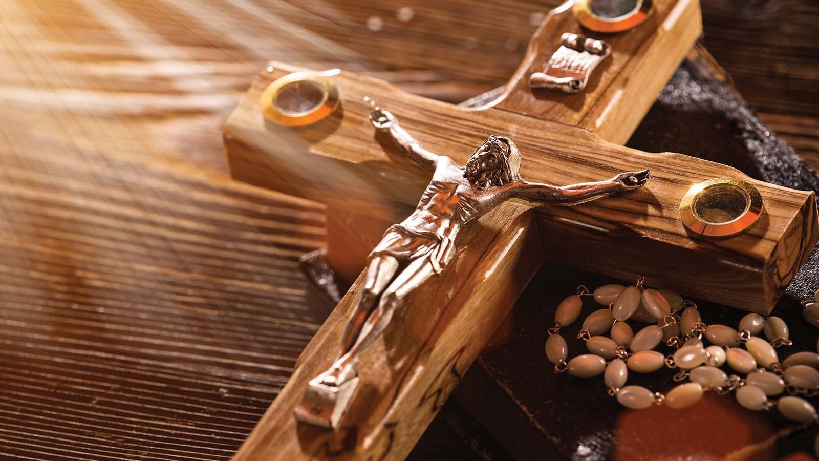 Sunlight shining on wooden crucifix and rosary setting on a wood table 